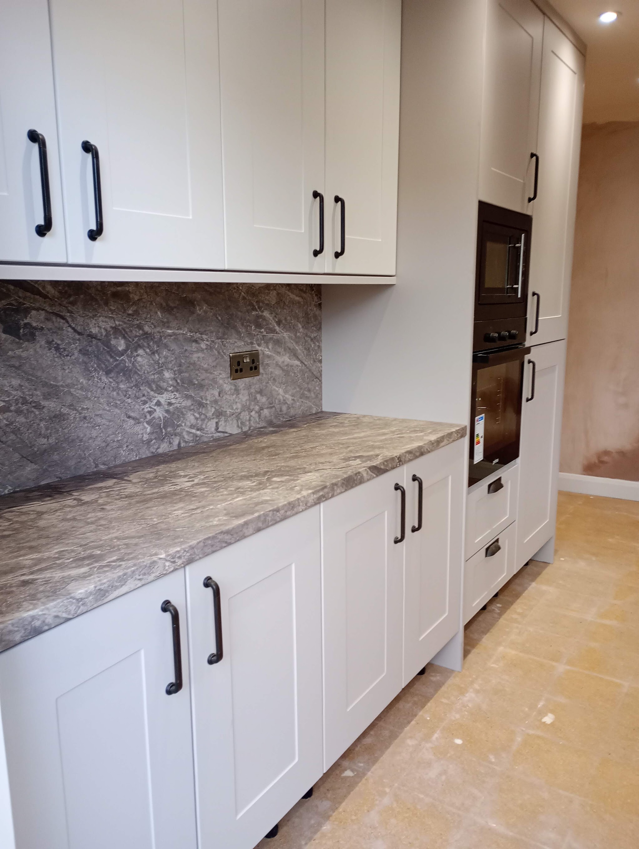 Newly fitted light grey kitchen with stone effect worktop and upstand
